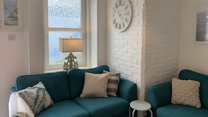 A living room with teal sofas, a white brick wall, a round clock, and a window with a frosted glass view. - Stunning 3-bed Apartment in Ventnor (Ventnor)