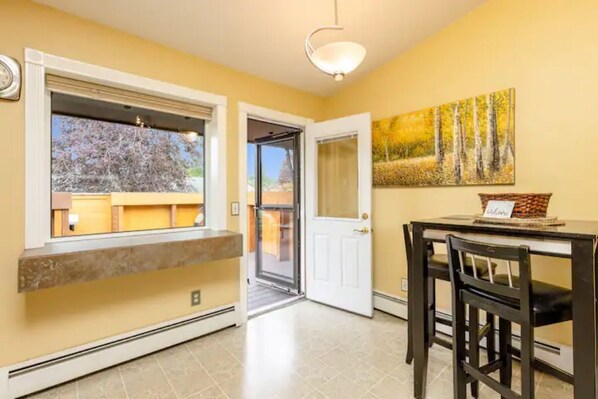 A room with a large window, a door, a table with chairs, and a painting on the wall. - Last Frontier Rental Family #D (Anchorage)