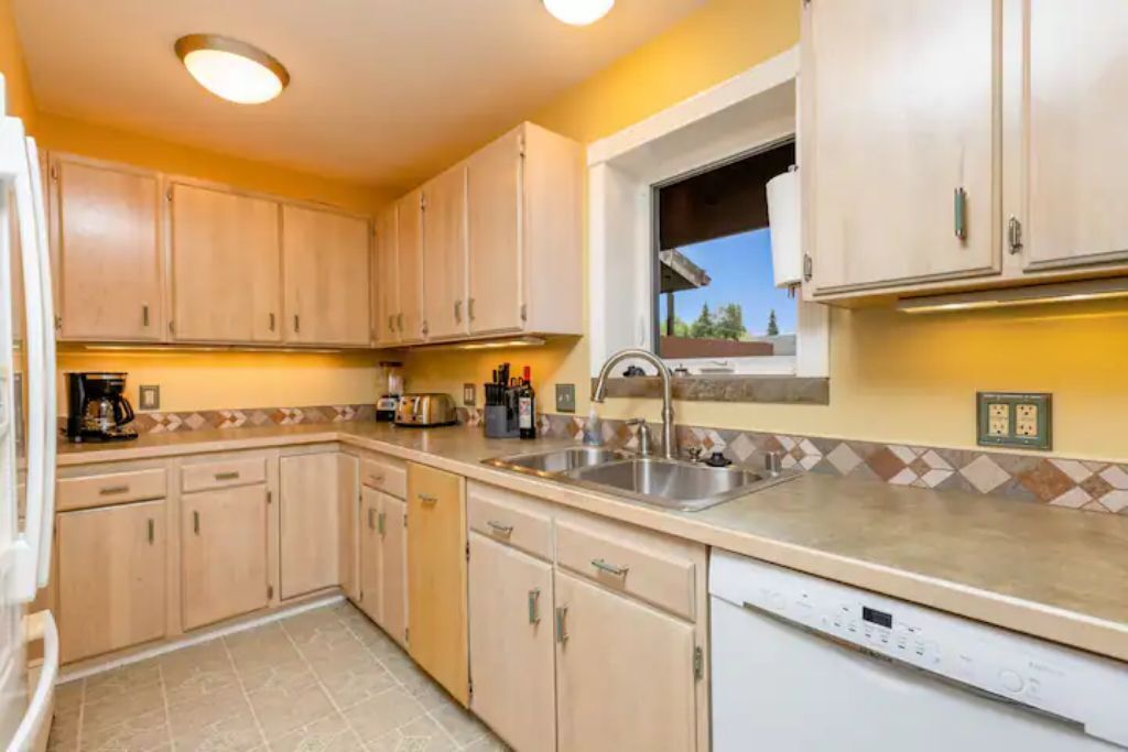 A kitchen with light wooden cabinets, a built-in dishwasher, and a window with a view of the outside.