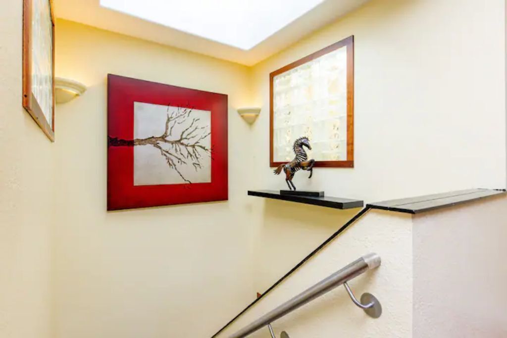 Una escala amb barana, una obra d'art amb marc vermell i una petita estant amb un objecte decoratiu.