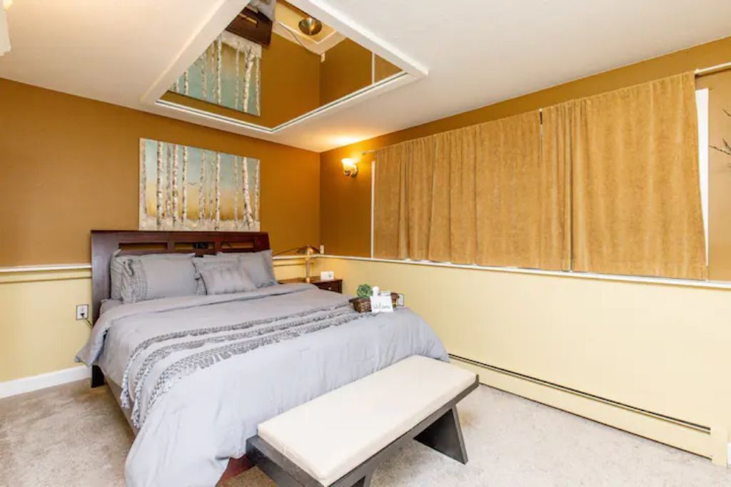 Een slaapkamer met een bed, een bankje en een raam met gordijnen.