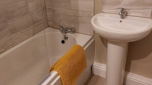 Ett badrum med badkar, ett vitt handfat och beige kakel på väggarna.