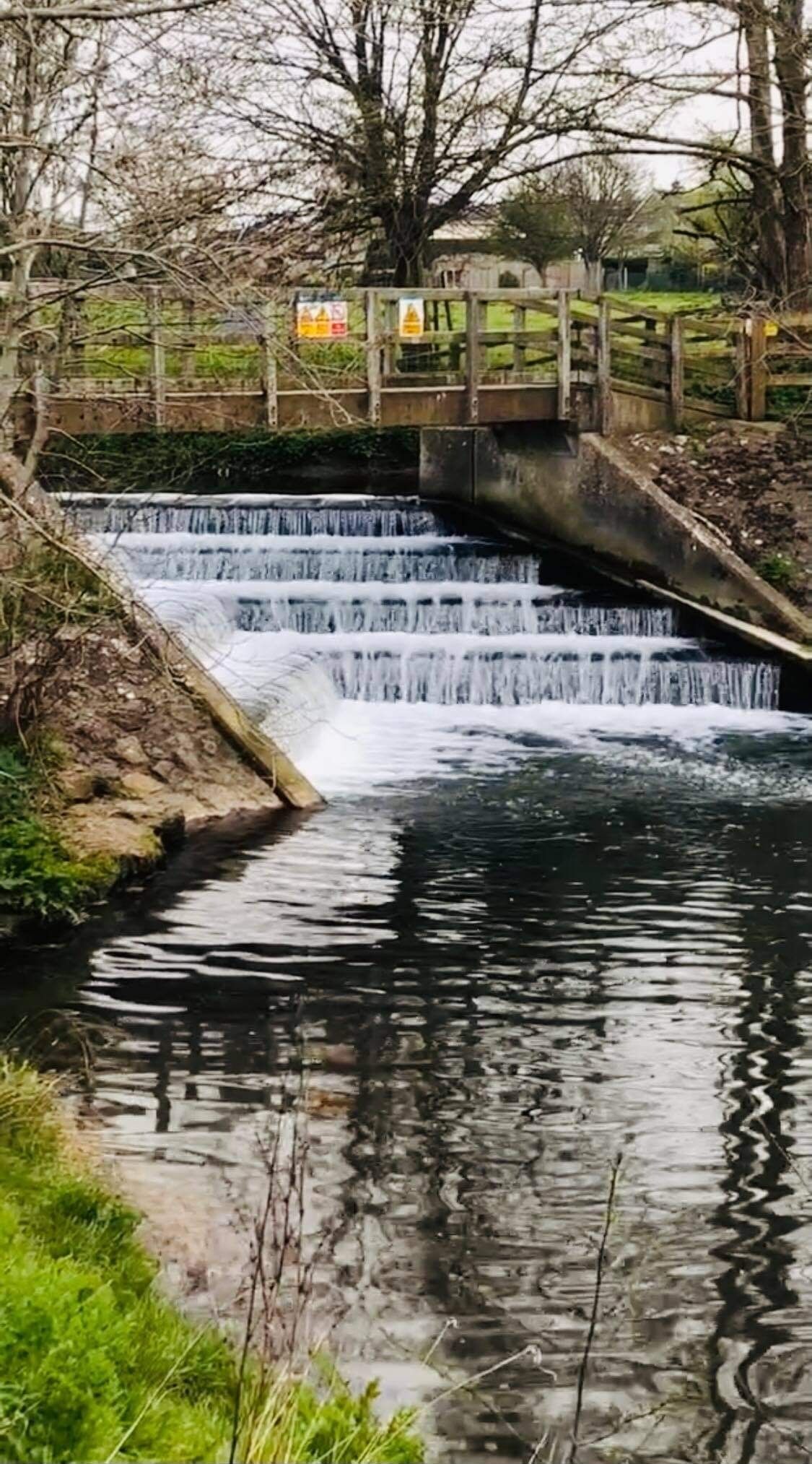 Une petite cascade dans un parc, avec un pont en bois et un mur de pierre.
