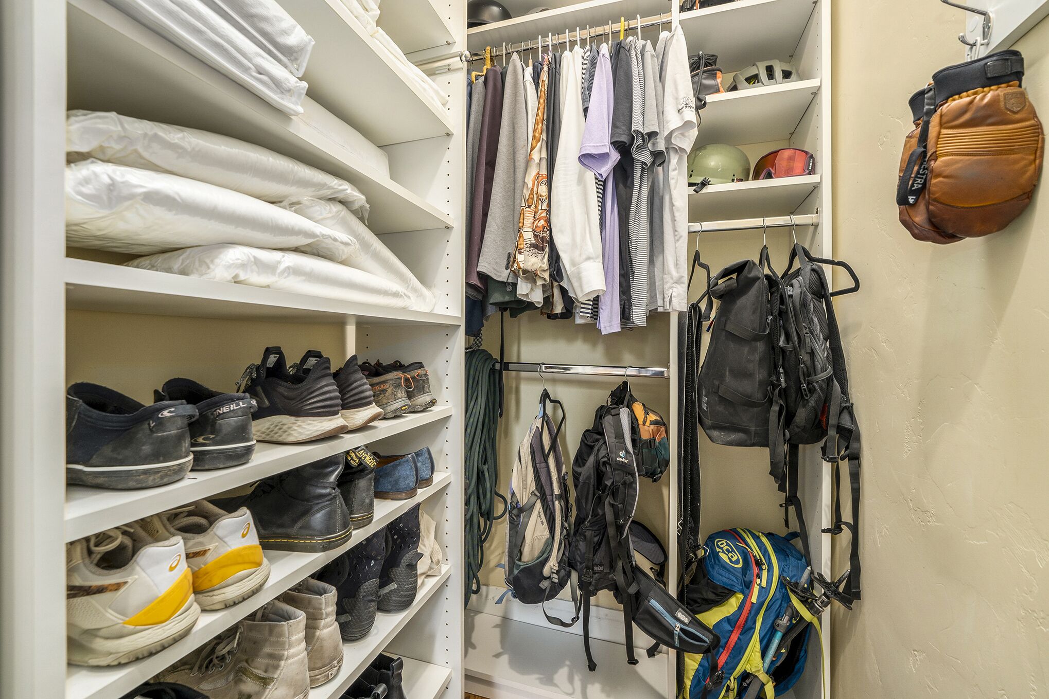 A closet with shelves of folded clothes, hanging garments, and various bags.