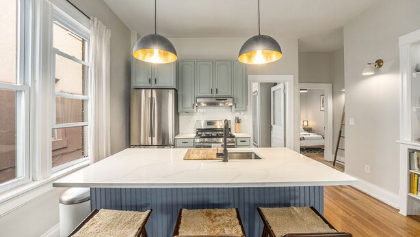 Cozinha moderna com ilha central, eletrodomésticos em aço inoxidável e iluminação pendente.