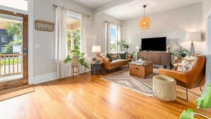 Uma sala de estar ampla com piso de madeira, um sofá, uma mesa de centro e uma televisão.
