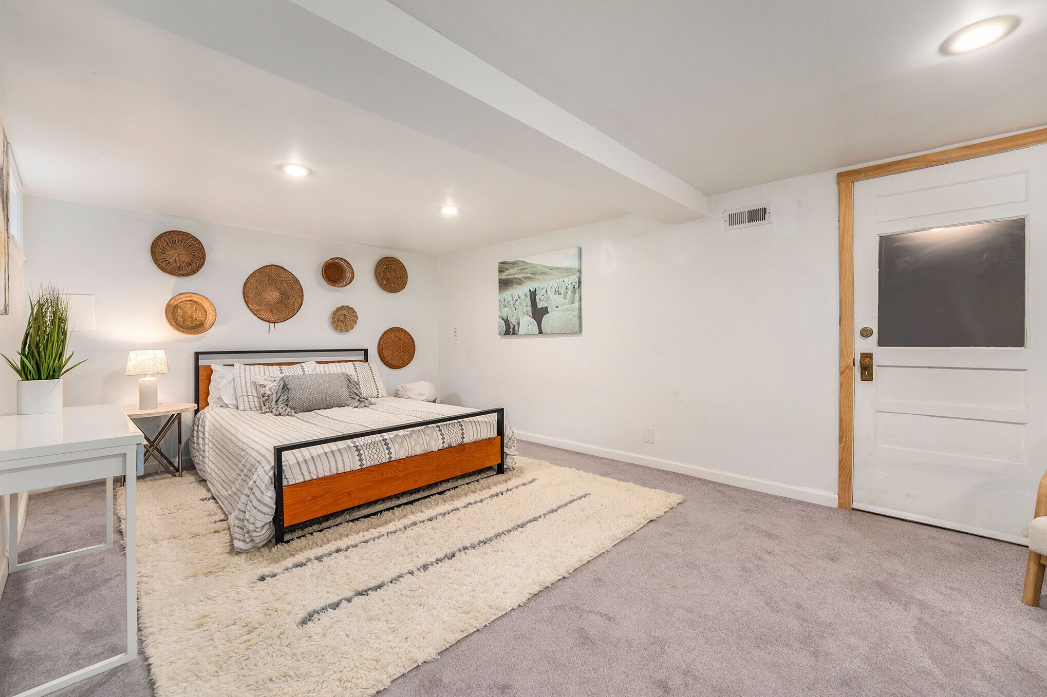 A bedroom with a bed, bedside tables, a rug, a wall-mounted artwork, and a door.