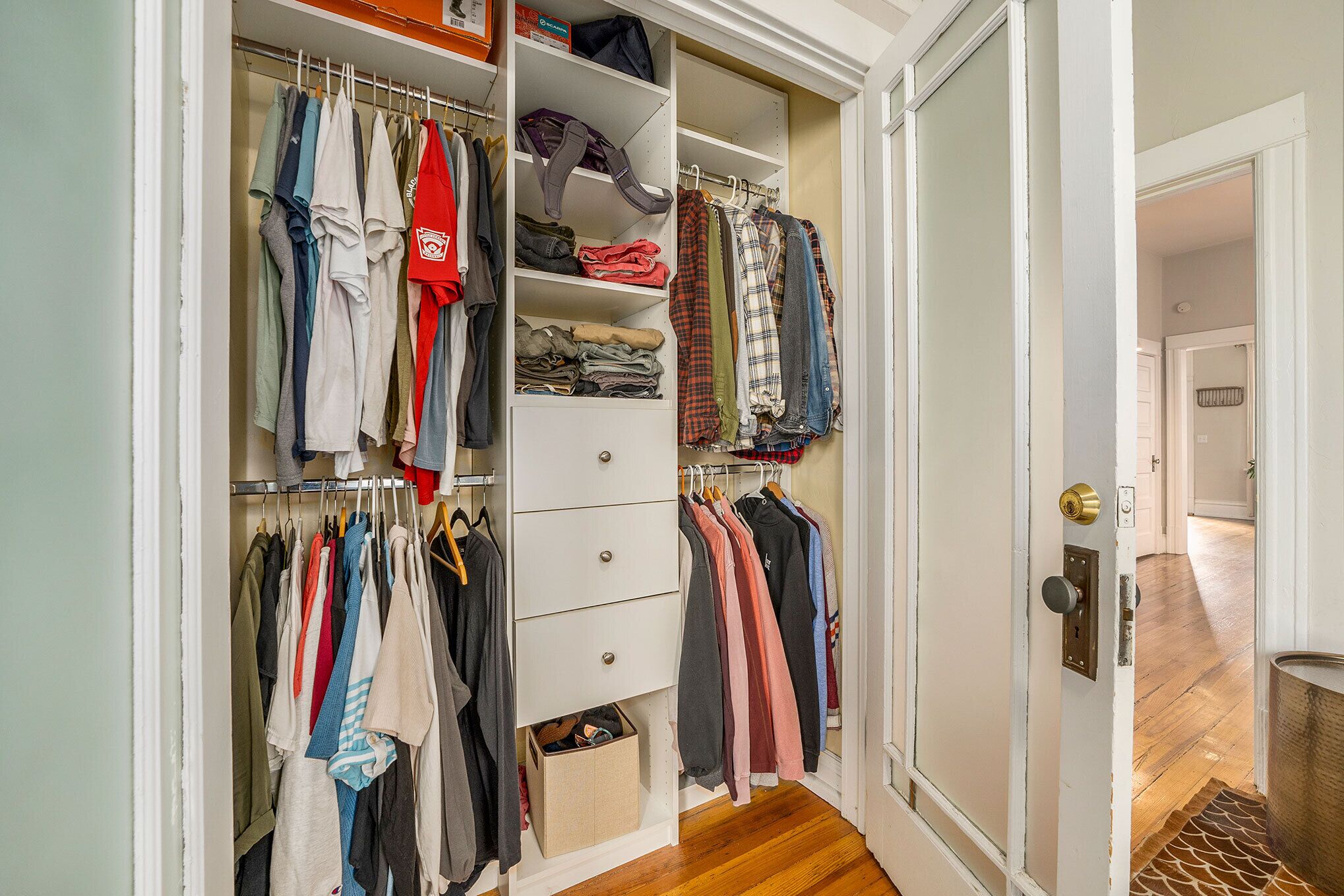Ein begehbarer Kleiderschrank mit hängender und gefalteter Kleidung, einem Schuhregal und einer kleinen Aufbewahrungsbox.