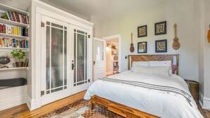 Quarto com cama de madeira, estante e porta com painéis de vidro jateado.