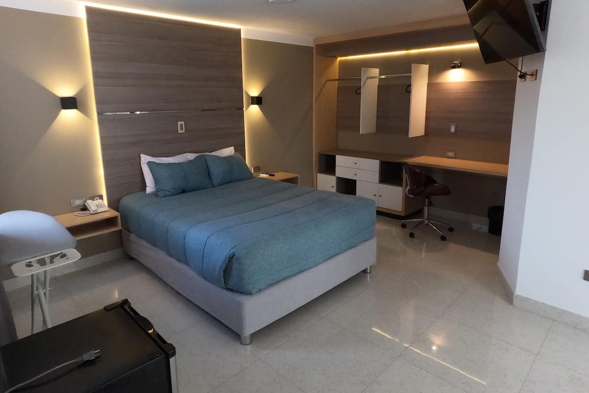Un dormitorio moderno con una cama, mesitas de noche, un escritorio y un televisor montado en la pared.