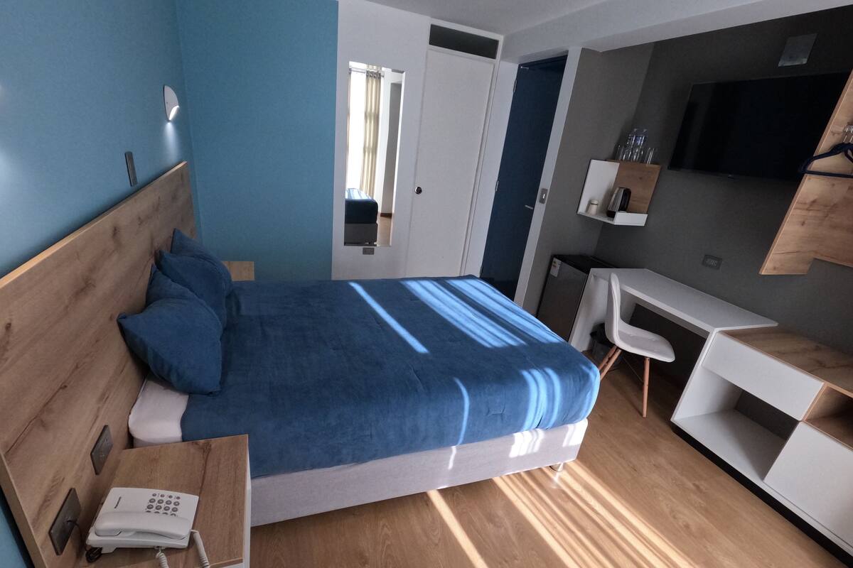Una habitación de hotel moderna con una cama de madera, un escritorio, una silla y un televisor fijado a la pared.