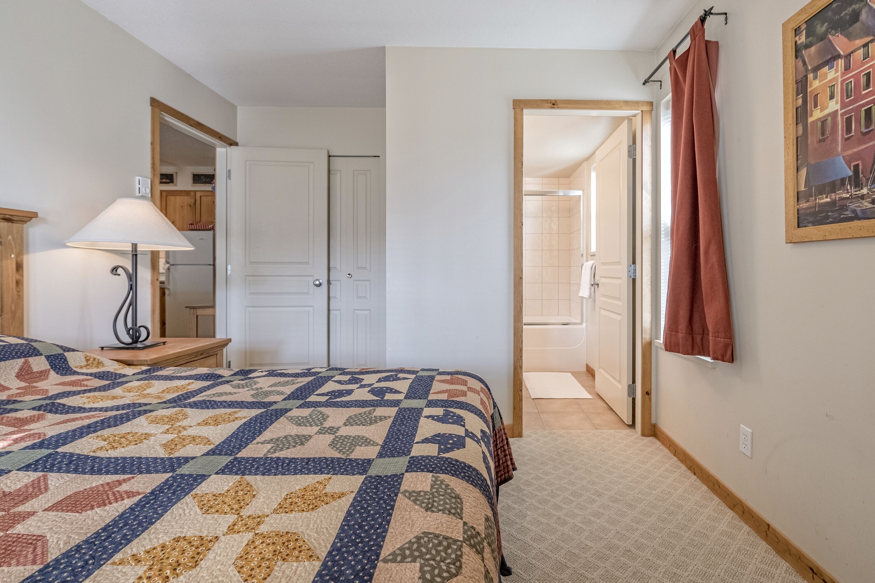 Un dormitorio con una cama grande, una mesita de noche, una lámpara y una puerta que da al baño.