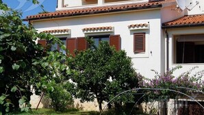 A two-story building with a balcony, satellite dish, and a garden with trees and shrubs. - Apartments Tea Medulin - One Bedroom Apartment with Terrace (Medulin)