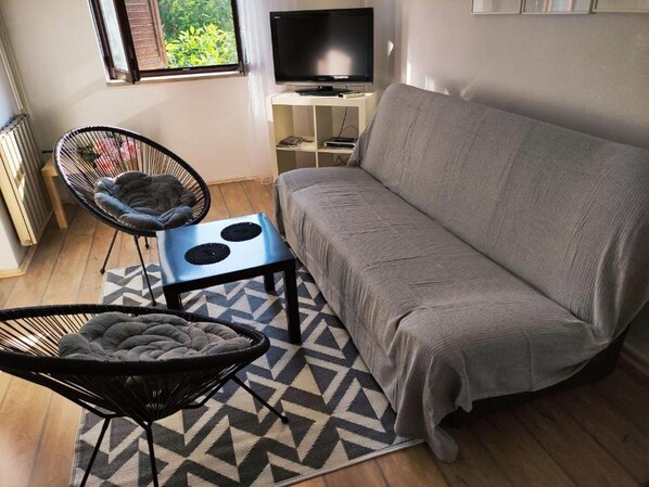 A compact living space with a sofa, a chair, a small table, and a TV.
