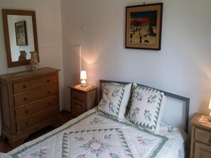 A bedroom with a bed, a dresser, a nightstand with a lamp, a painting on the wall, and a mirror above the dresser.