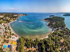 An aerial view of a coastal area with a beach, clear waters, and a small island.