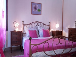 Um quarto com uma cama, duas mesas de cabeceira, um criado-mudo, uma luminária e um quadro na parede.