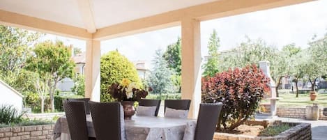 An outdoor patio with a table and chairs, surrounded by a garden with various plants and trees.