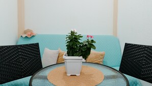 Ein runder Glastisch mit einer gewebten Tischunterlage, ein weißer Topf mit Grünpflanzen und ein türkisfarbenes Sofa mit Kissen.