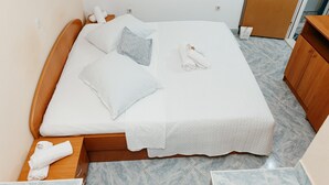Un letto ben rifatto con lenzuola bianche, una testiera in legno e un pavimento in marmo.