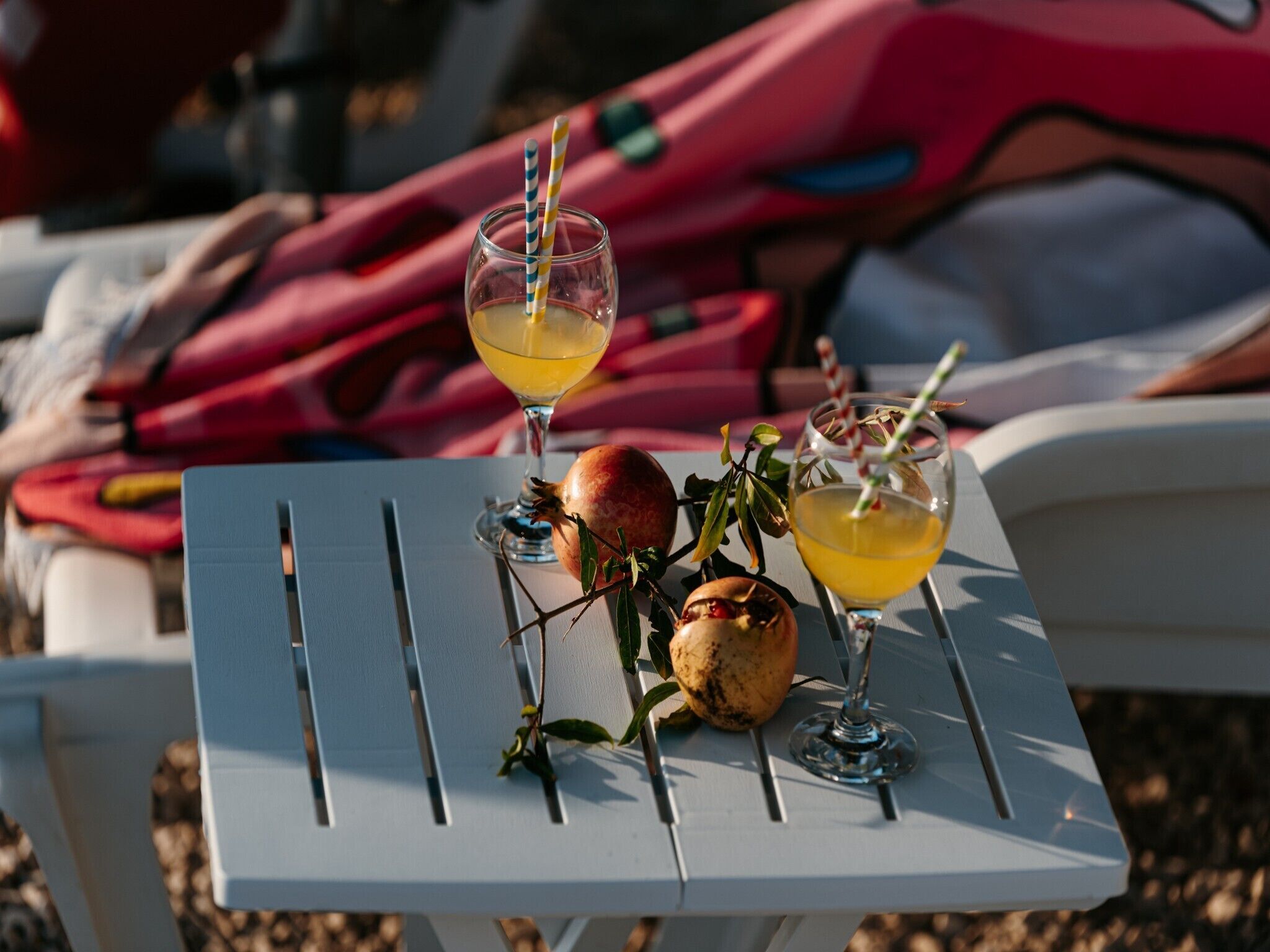 A table with two glasses of a yellow beverage, a pomegranate, and a branch with leaves.