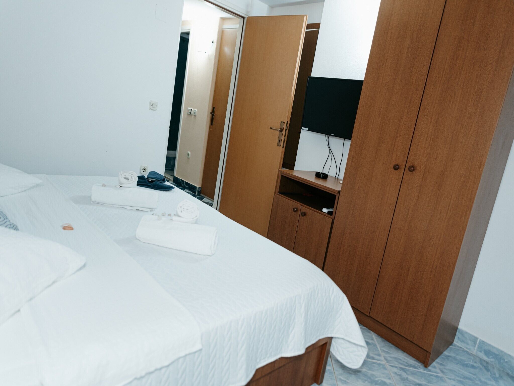 A hotel room with a bed, a wooden wardrobe, a mirror, and a television.