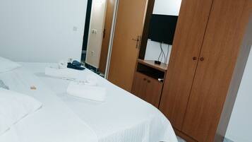 A hotel room with a bed, a wooden wardrobe, a mirror, and a television.