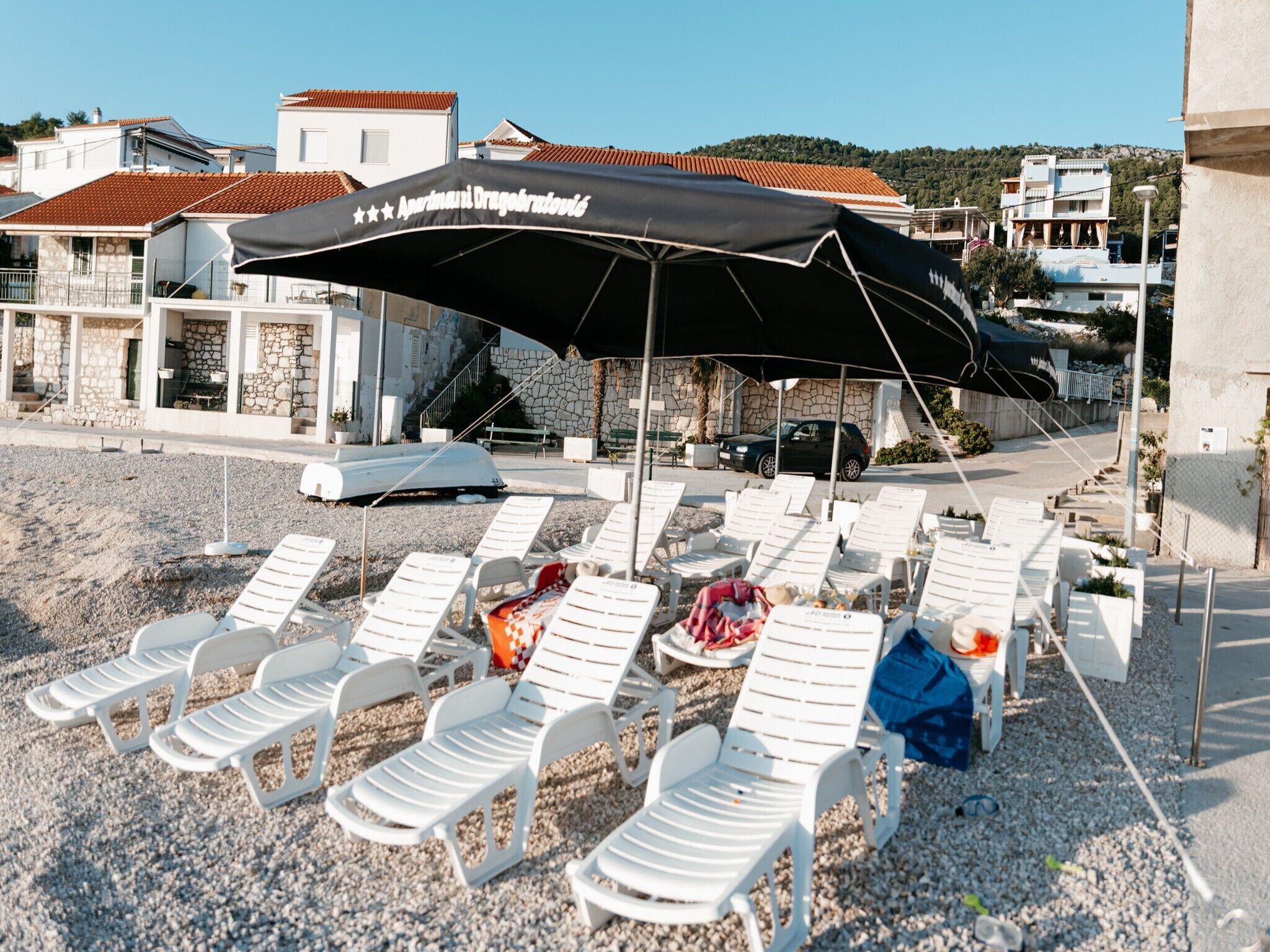 A beachside area with white lounge chairs and a black umbrella.