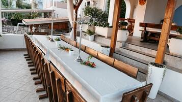 An outdoor dining area with a long table, wooden chairs, and potted plants.