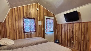 A small, cozy room with wooden walls and a sloped ceiling. There are two beds with matching bedding, a flat-screen TV mounted on the wall, and a window with patterned curtains. - Blackhills Cabin 2 Twin Beds in Sturgis, SD.Close to Downtown, Deadwood, Spearfish and Mt. Rushmore (Sturgis)