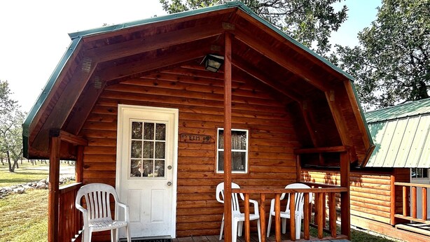 A wooden cabin with a porch, a door, and a bench. - Blackhills Cabin 2 Twin Beds in Sturgis, SD.Close to Downtown, Deadwood, Spearfish and Mt. Rushmore (Sturgis)
