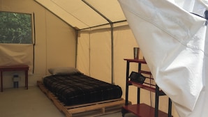 Ein Zelt mit Bett, einem kleinen Tisch und einem Regal mit Büchern.