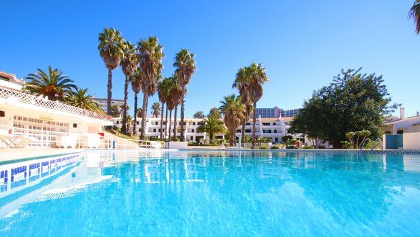 A swimming pool with clear blue water, surrounded by palm trees and hotel buildings. - Villa with pool access & BBQ, Albufeira (Albufeira)