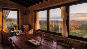 Zona pranzo con tavolo in legno, sedie e vista sulla campagna attraverso ampie finestre.