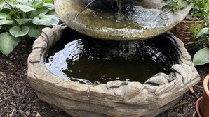 A tiered stone water feature with cascading water, surrounded by lush greenery and a wooden fence. - Hot tub, fire pit, great outdoor space, by Coler bike trails, Bentonville Square (Bentonville)