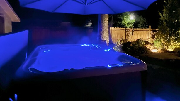 A hot tub with a blue-lit umbrella, surrounded by a wooden fence and trees. - Hot tub, fire pit, great outdoor space, by Coler bike trails, Bentonville Square (Bentonville)