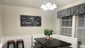 A kitchen with a dark wooden table, two bar stools, a potted plant, and a wall-mounted sign reading "Coffee Bar". - Hot tub, fire pit, great outdoor space, by Coler bike trails, Bentonville Square (Bentonville)