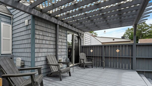 A covered deck with Adirondack chairs and a table, wooden siding walls, and a pergola structure. - Dog-Friendly Norfolk Cottage Near Ocean View Beach (Norfolk)