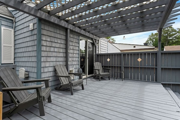 A covered deck with Adirondack chairs and a table, wooden siding walls, and a pergola structure.
