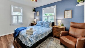 A bedroom with a bed, two bedside tables, a ceiling fan, a brown leather chair, and a window. - Dog-Friendly Norfolk Cottage Near Ocean View Beach (Norfolk)