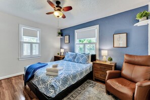 A bedroom with a bed, two bedside tables, a ceiling fan, a brown leather chair, and a window. - Dog-Friendly Norfolk Cottage Near Ocean View Beach (Norfolk)