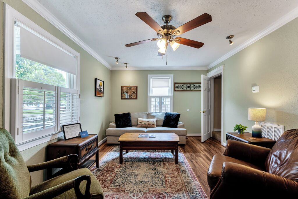 Un salon avec un ventilateur de plafond, un canapé, une table basse et un fauteuil.