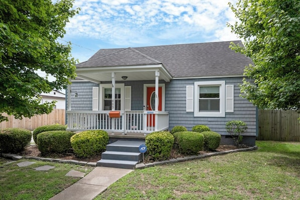 A residential house with a porch, a front door, and a small front yard with trimmed bushes.