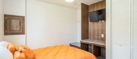 Ein Schlafzimmer mit einem Bett, einem Deckenventilator, einem an einer Holzwand montierten Fernseher und einem weißen Kleiderschrank.