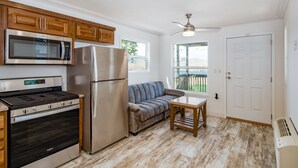 Una cocina con estufa, microondas, refrigerador, armarios de madera y una ventana.