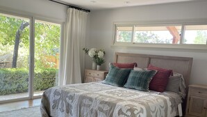 Quarto com uma cama grande, uma mesa de cabeceira, uma janela com cortinas e vista para o verde lá fora.