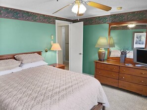 Ein Schlafzimmer mit einem Bett, einem Schminktisch, einem Fernseher und einem Deckenventilator.
