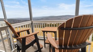 A balcony with two wooden Adirondack chairs and a small table, overlooking a hilly landscape.