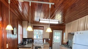 Une cuisine aux murs lambrés, avec une table à manger, des chaises, des luminaires suspendus et un réfrigérateur.
