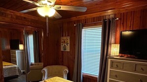 Une pièce de style cabane en bois, comprenant un lit, une chaise, une commode et un ventilateur de plafond.
